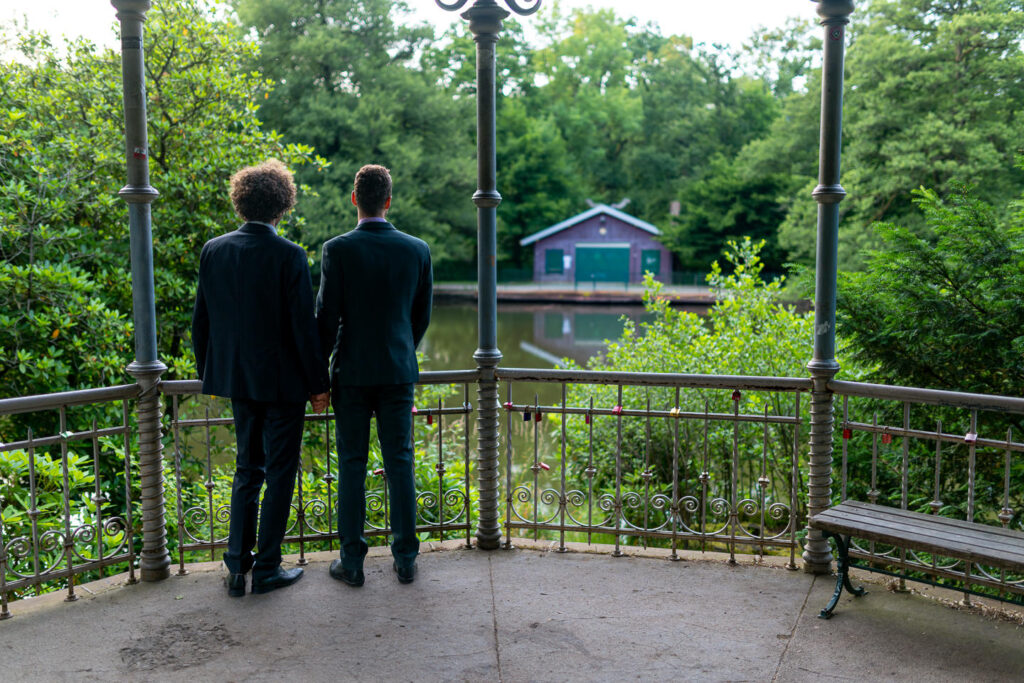 Verlobungspaar an Aussichtsplattform Waldsee Freiburg blickt auf grüne Waldlandschaft mit türkisfarbenem Haus.