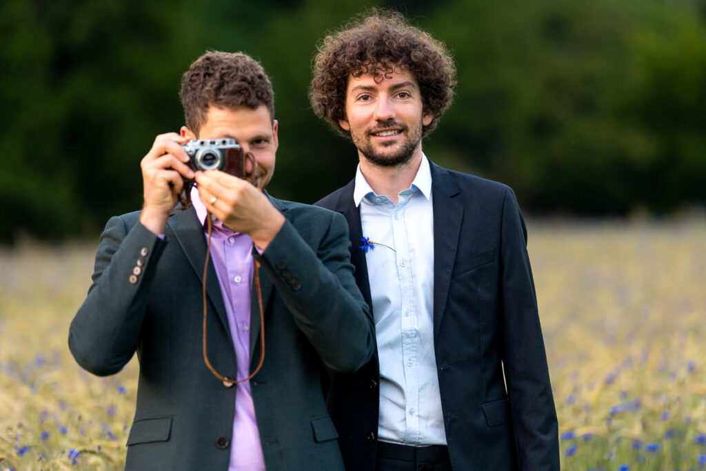 Zwei Männer beim Verlobungsshooting im gelben Blumenfeld, einer mit Vintage-Kamera, Freiburg Waldsee.