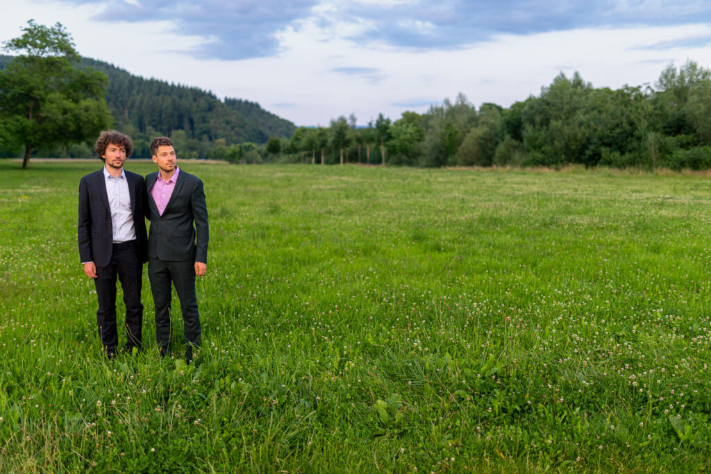 Verlobtes Paar in eleganter Kleidung auf weitläufiger grüner Wiese bei Freiburg im Frühling.