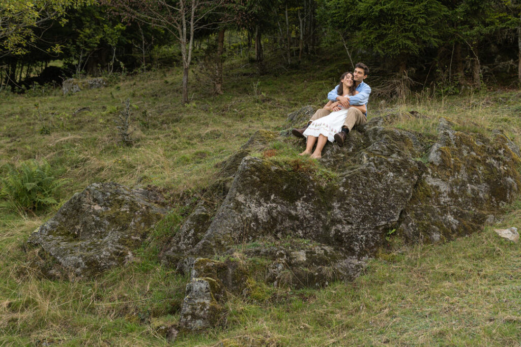 Braut im weißen Hochzeitskleid entspannt auf Felsen in grüner Naturlandschaft beim romantischen Paarshooting.