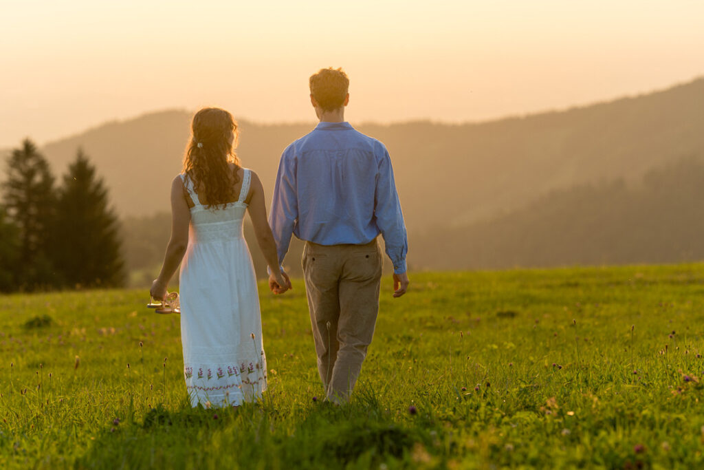 Brautpaar Hand in Hand auf Bergwiese im Schwarzwald bei goldenem Sonnenuntergang mit Bergpanorama.