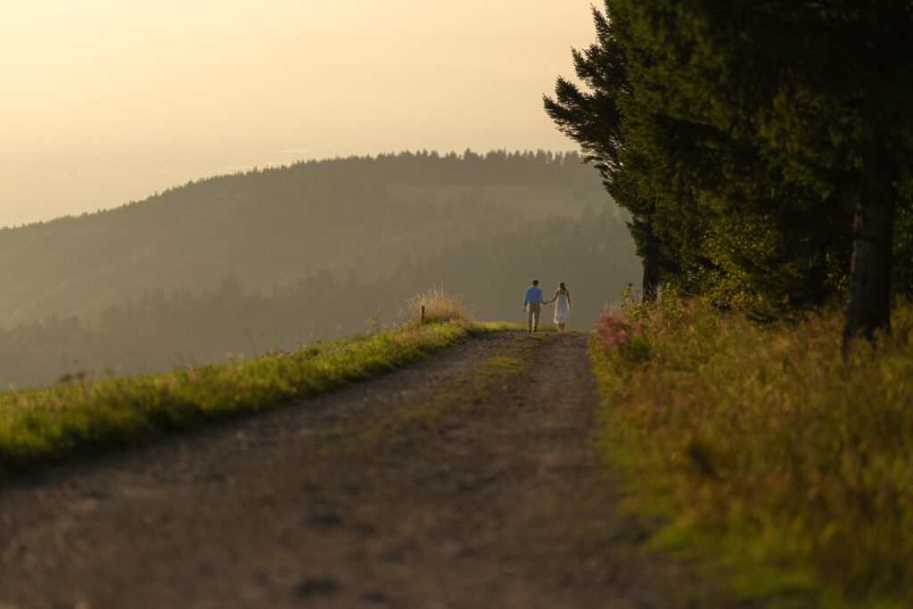 Brautpaar auf Feldweg bei goldenem Sonnenuntergang in romantischer Hügellandschaft.