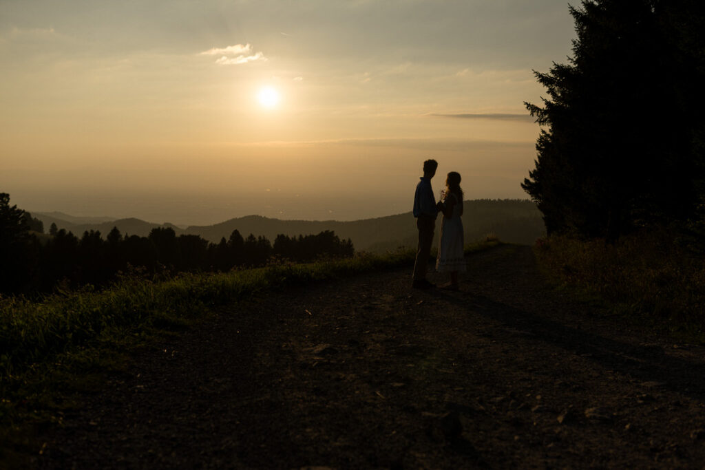 Brautpaar-Silhouette bei goldenem Sonnenuntergang auf ländlichem Feldweg mit romantischer Atmosphäre.