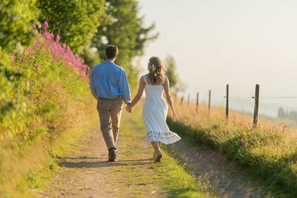 Brautpaar Hand in Hand auf romantischem Feldweg im goldenen Sonnenlicht bei Sonnenuntergang.