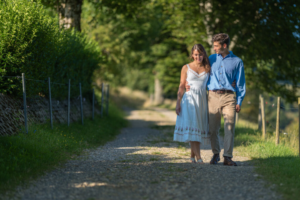 Brautpaar spaziert romantisch auf sonnigem Landweg zwischen grünen Bäumen im Freien.
