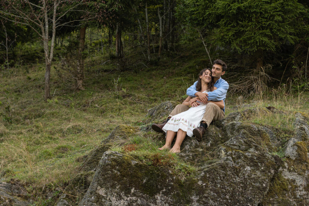 Verliebtes Paar auf moosbedecktem Felsen im grünen Nadelwald bei natürlichem Licht.