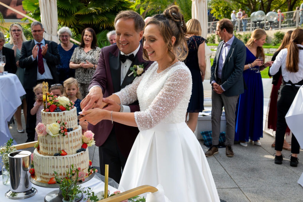 Brautpaar schneidet Hochzeitstorte im Freien an, Gäste beobachten die Zeremonie im Wilden Mann Meersburg.