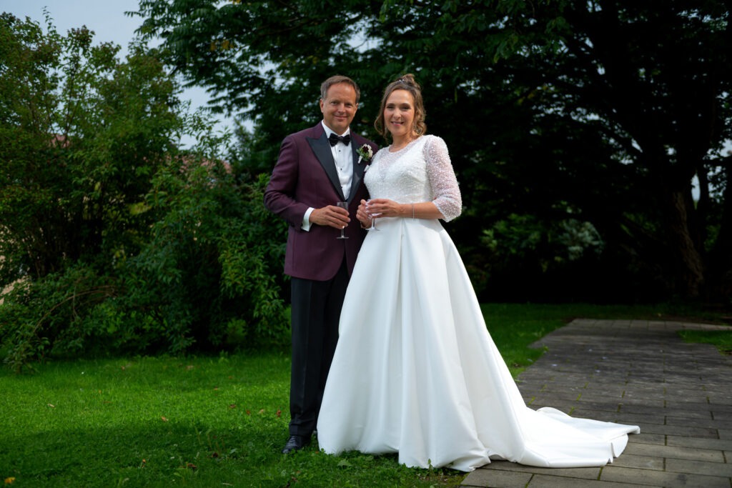 Elegantes Brautpaar in weißem Kleid und dunklem Anzug in der Grünen Allee Konstanz.