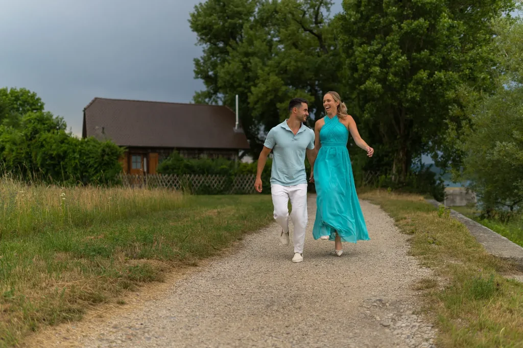 Engagement Svenja und Yannik laufen Hand in Hand lachend über einen Kiesweg.